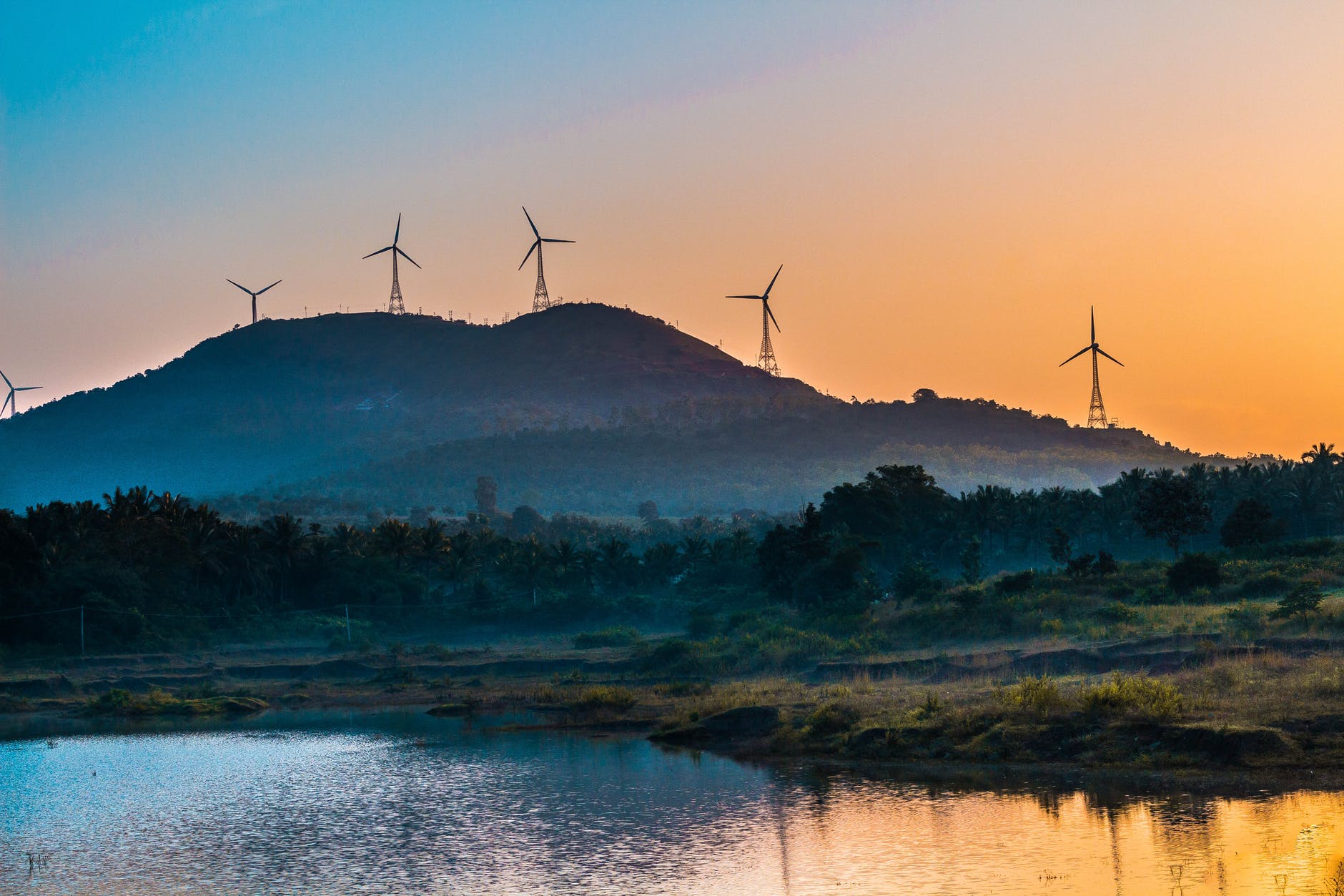 windmills in mountain viewing lake under orange skies