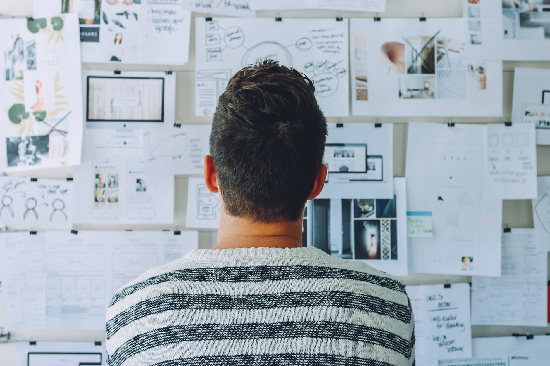 man wearing black and white stripe shirt looking at white printer papers on the wall