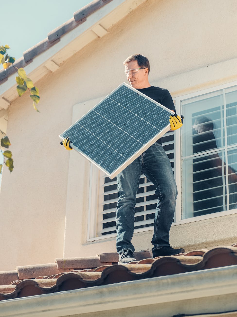 a man in black shirt standing on the roof while holding a solar panel